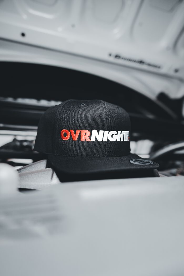 Close-up of a stylish black cap with "OVRNIGHT" text displayed on a sleek automobile background.