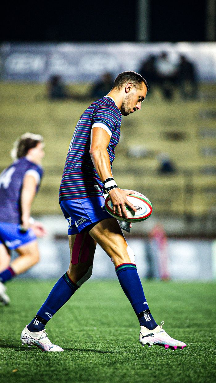 Rugby player holding the ball during a competitive night match on the field.
