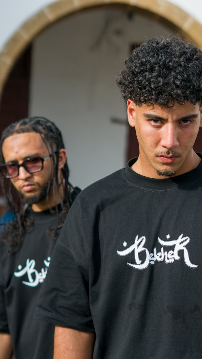 Two young men pose wearing black t-shirts with logo design, outdoors in Morocco.